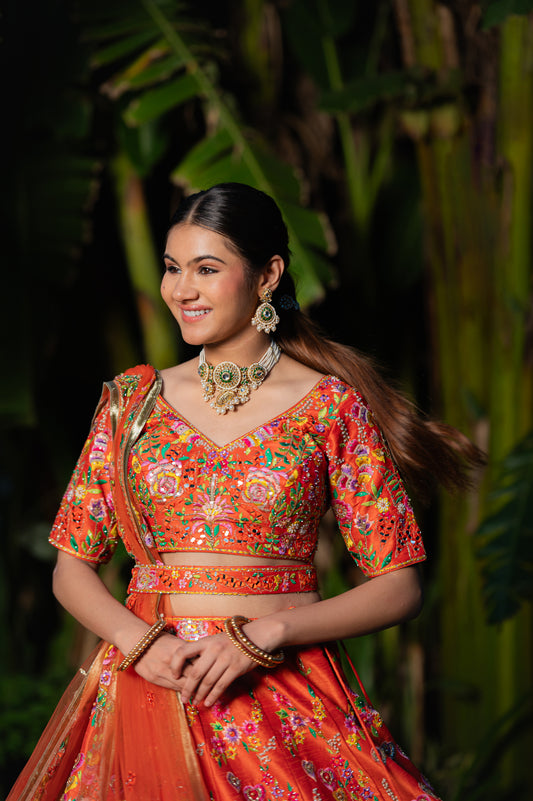A stunning orangy red raw silk lehenga featuring thread sequins and moti work lehenga beautifully adorned with fine craftsmanship and exquisite detailing, perfect for festive and special occasions.
